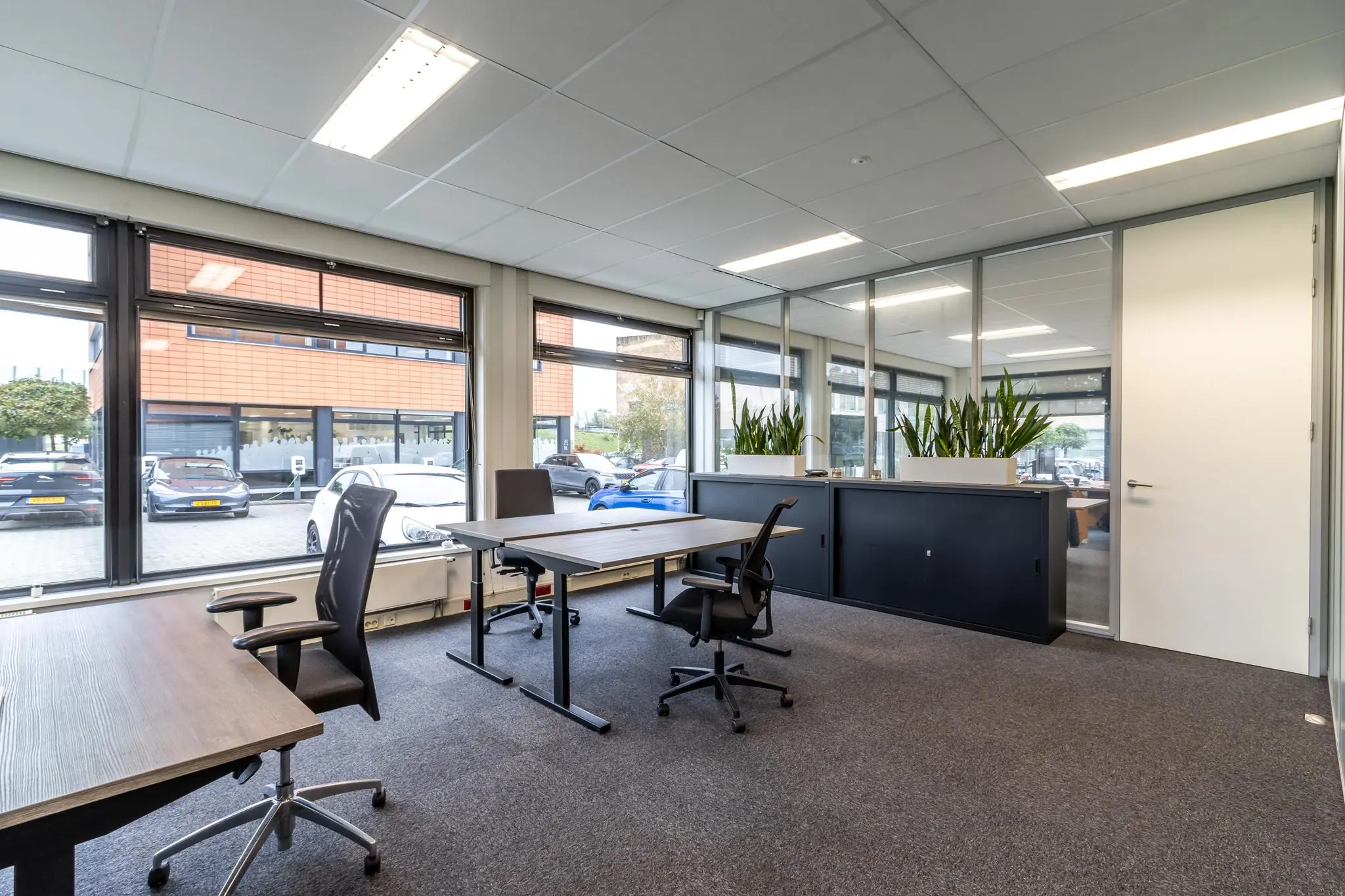 Licht en modern kantoor aan de Lage Biezenweg met werkplekken, plantenbakken en uitzicht op de parkeerplaats.